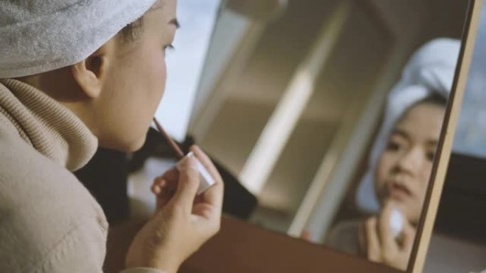 美丽的亚洲女人正在化妆，并在家里的镜子前使用化妆品作为她的日常美容。