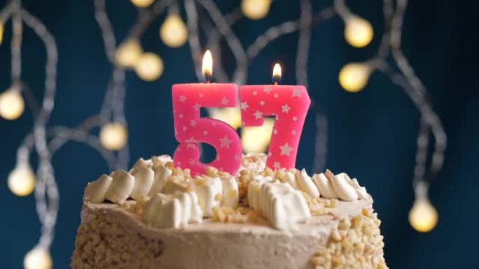 蓝色背景上有57号粉色蜡烛的生日蛋糕。蜡烛吹灭了。慢动作和特写视图