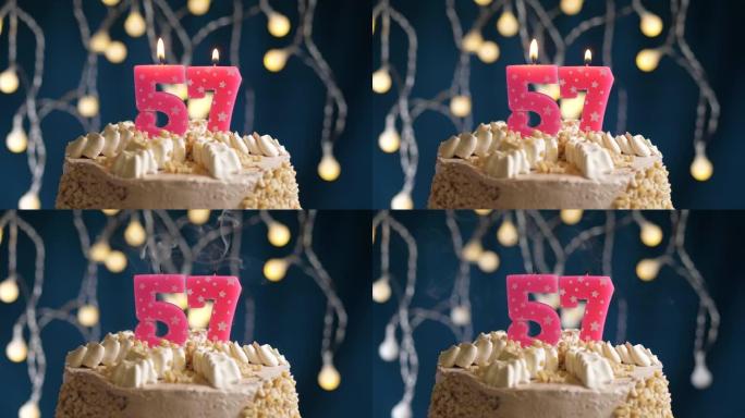 蓝色背景上有57号粉色蜡烛的生日蛋糕。蜡烛吹灭了。慢动作和特写视图