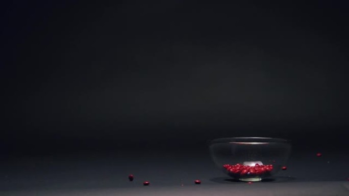 红色糖果在慢动作中掉落在玻璃碗中，黑色黑板纹理背景上的复制空间
