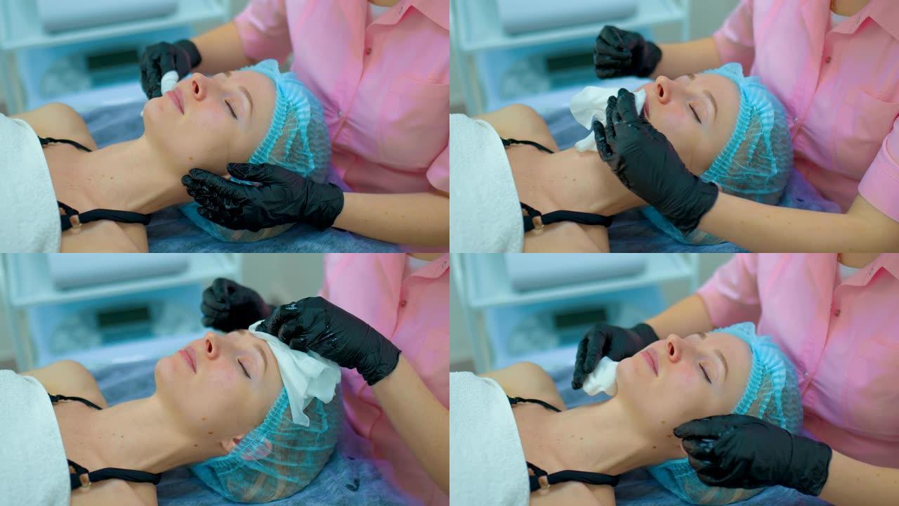 整容手术后，年轻女子用餐巾纸擦脸。美容师把面膜从女人脸上洗掉。肖像视图。