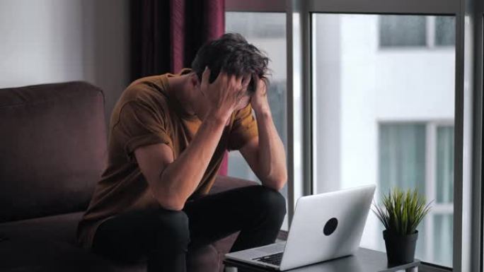 男人对笔记本电脑屏幕上看到的坏消息感到不愉快的惊讶和震惊。男人坐在家里的客厅靠窗时，承受着压力和绝望