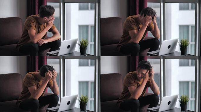 男人对笔记本电脑屏幕上看到的坏消息感到不愉快的惊讶和震惊。男人坐在家里的客厅靠窗时，承受着压力和绝望
