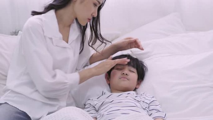 年轻的亚洲母亲手照顾和检查她的儿子发热体温，生病的男孩睡在床上，女人担心冠状病毒流感，医疗保健和预防
