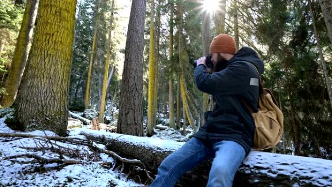 一位大胡子的男性旅行者摄影师在冬季森林中拿着相机拍摄大自然的照片。博客作者和摄影艺术家的旅行概念