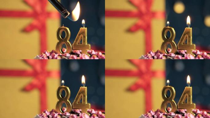 生日蛋糕编号84点灯燃烧的金色蜡烛，蓝色背景礼物黄色盒子用红丝带绑起来。特写和慢动作