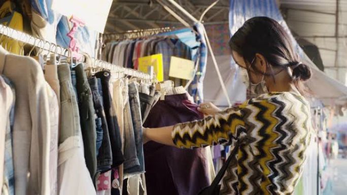 亚洲妇女在泰国市场上挑选，选择和购买带有口罩的衣服。