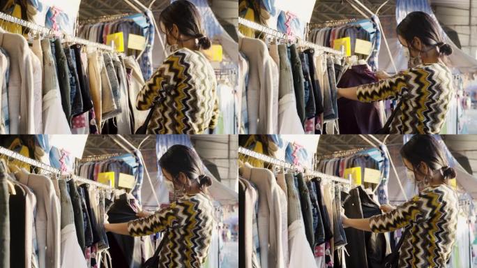 亚洲妇女在泰国市场上挑选，选择和购买带有口罩的衣服。