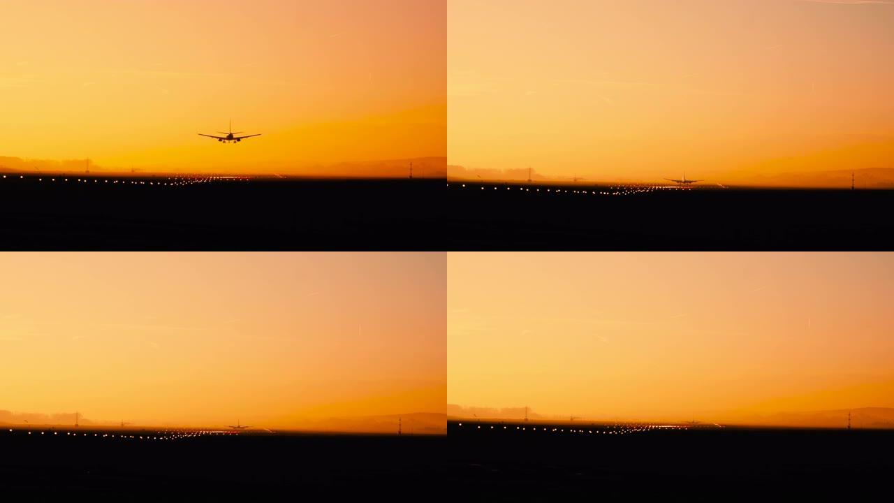 在阳光明媚的橙色和紫色日落时，飞机降落在机场的后视图轮廓。跑道末端识别灯和频闪发光。