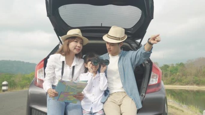 亚洲家庭的肖像坐在车里，父亲指着风景，母亲拿着地图，女儿在度假时用双筒望远镜看着美丽的风景。幸福的家