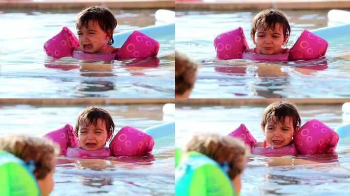 心烦意乱的小女孩在游泳池水中蹒跚学步，抱怨穿着漂浮物