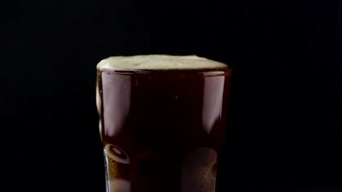 酒保将黑啤酒从瓶子倒入玻璃杯中。一个男人在杯子里装满黑啤酒。