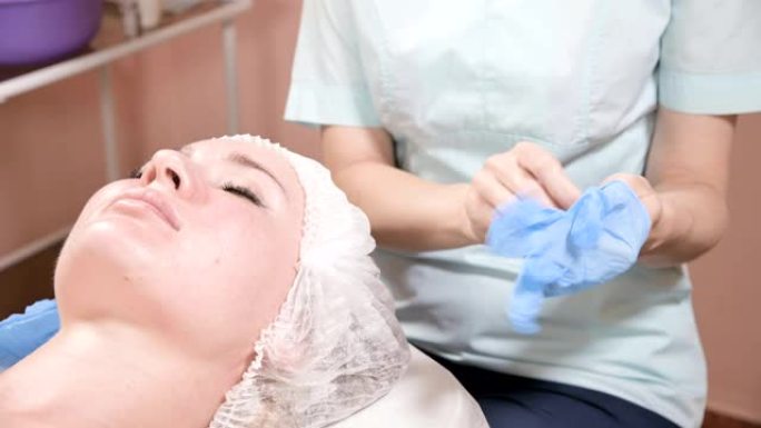 专业女性美容师在进行客户面部美容护肤程序之前，先戴上蓝色橡胶清洁无菌手套。美容专业的概念