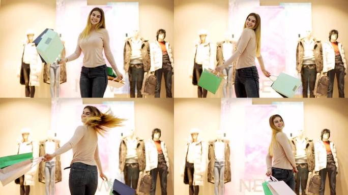 快乐的金发年轻女子带着购物袋在慢动作中快乐地跳舞，看着摄像机站在商场橱窗展示附近，庆祝购物成功