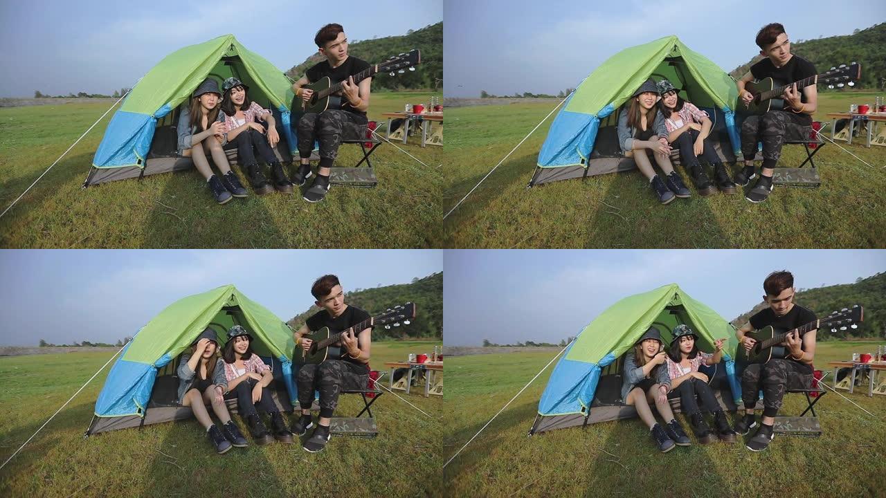 一群亚洲朋友的游客在夏天在日落时在湖边露营时与快乐一起喝酒和弹吉他