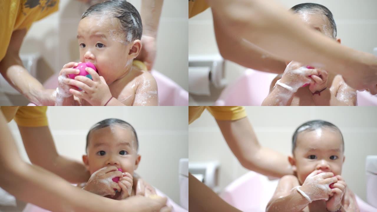 一个男婴在粉红色的浴缸里洗澡和咬玩具。