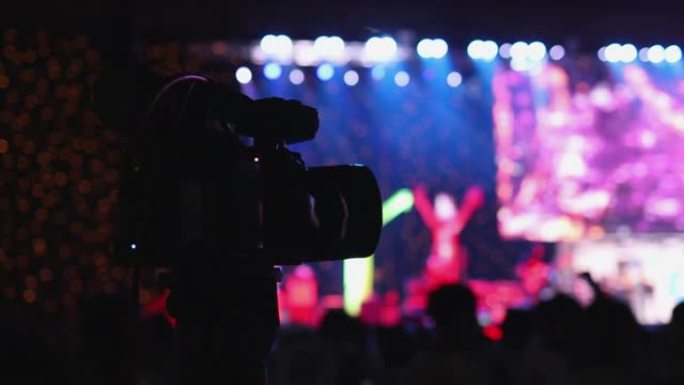 慢动作，人们聚会的剪影，摄像师在大厅的舞台前录制视频摇滚音乐会。彩色蓝色舞台灯光，带led灯的舞台聚