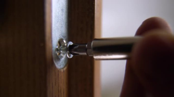 木匠修理门锁的特写。安装门把手。杂工拧紧门铰链。修理工用螺丝刀的手。锁匠将螺栓拧入木门