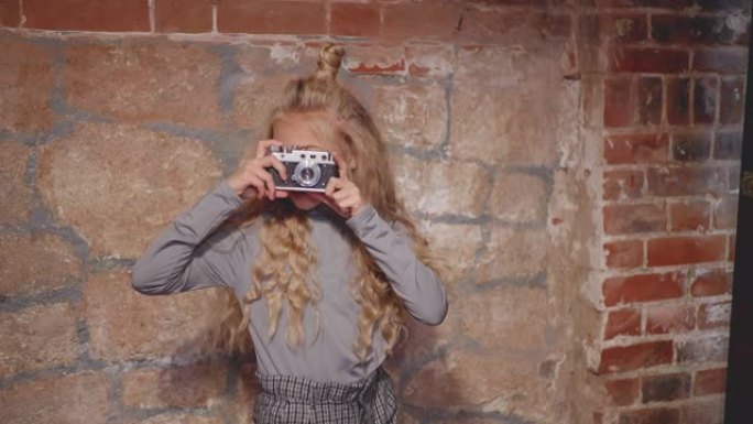 时髦女孩在砖墙背景上的老式相机上摄影。年轻女孩在砖背景上的照相馆使用复古相机。