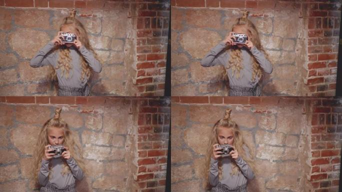 时髦女孩在砖墙背景上的老式相机上摄影。年轻女孩在砖背景上的照相馆使用复古相机。