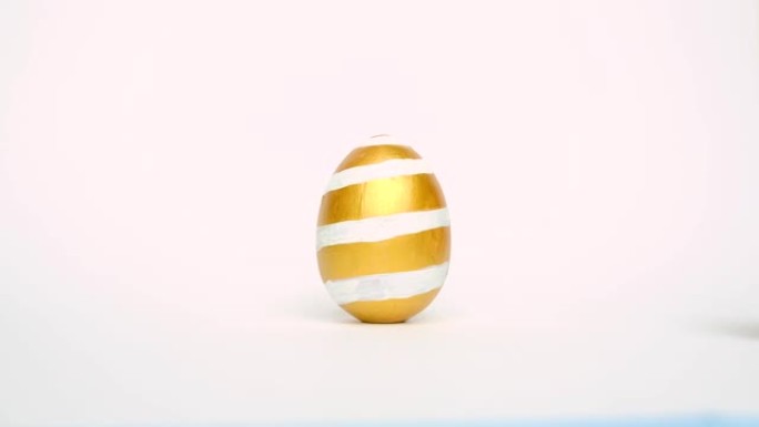 复活节彩蛋在滚动，互相敲在白色的桌子上。鸡蛋时尚彩色经典蓝色、白色和金色。复活节快乐。最小风格