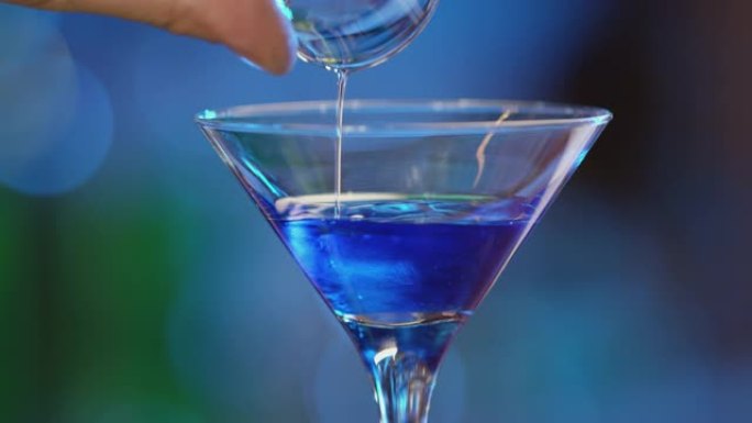 专业酒保用冰装饰蓝色鸡尾酒。调酒师在散焦的背景下准备鸡尾酒，然后倒入并提供鸡尾酒。酒保准备五颜六色的