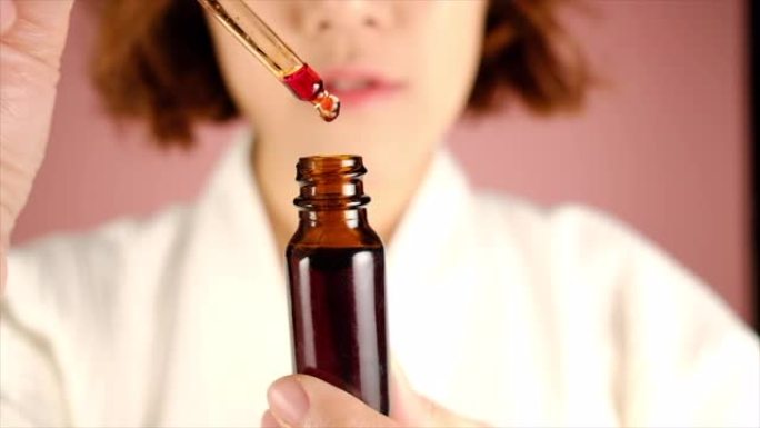 女人将红色血清或药物放入琥珀色小瓶中。美容护肤和保健理念。