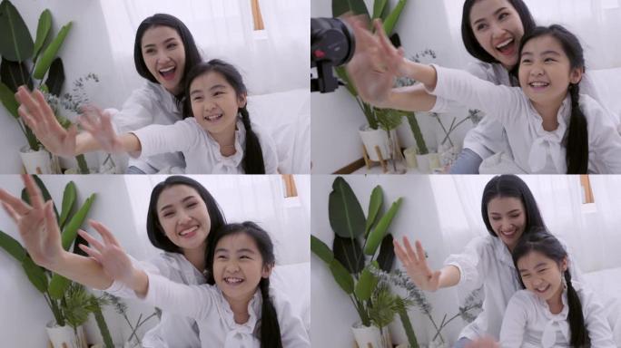 快乐的亚洲母女挥手向相机打招呼或再见，顽皮的女人和可爱的女孩在家里给家人或父亲的视频通话前玩耍，社交