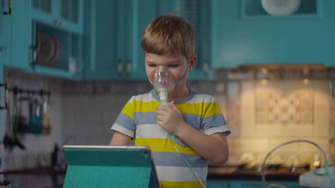 小男孩使用吸入器治疗流感或呼吸道病毒等疾病，在家观看平板电脑。厨房用药物吸入器面罩治疗咳嗽的孩子 .