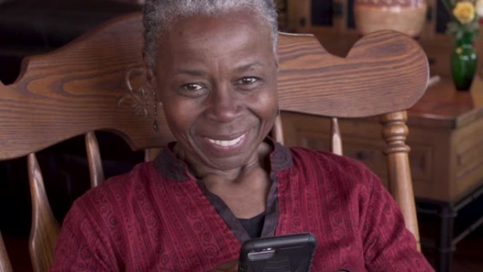 快乐的高级黑人女性使用手机抬头看着相机微笑