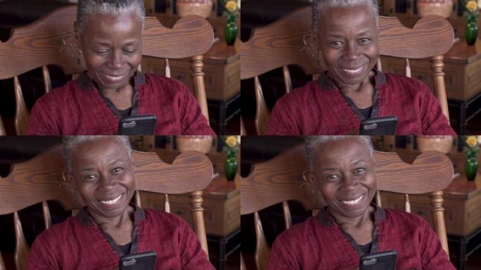 快乐的高级黑人女性使用手机抬头看着相机微笑