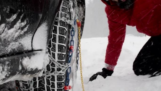 下雪时雪路上的冬季轮胎。英俊活跃的高级男子戴上轮胎链。冬季条件下的道路安全。