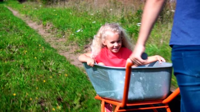 快乐的年轻成年母亲和小女儿在花园独轮车上快速骑行