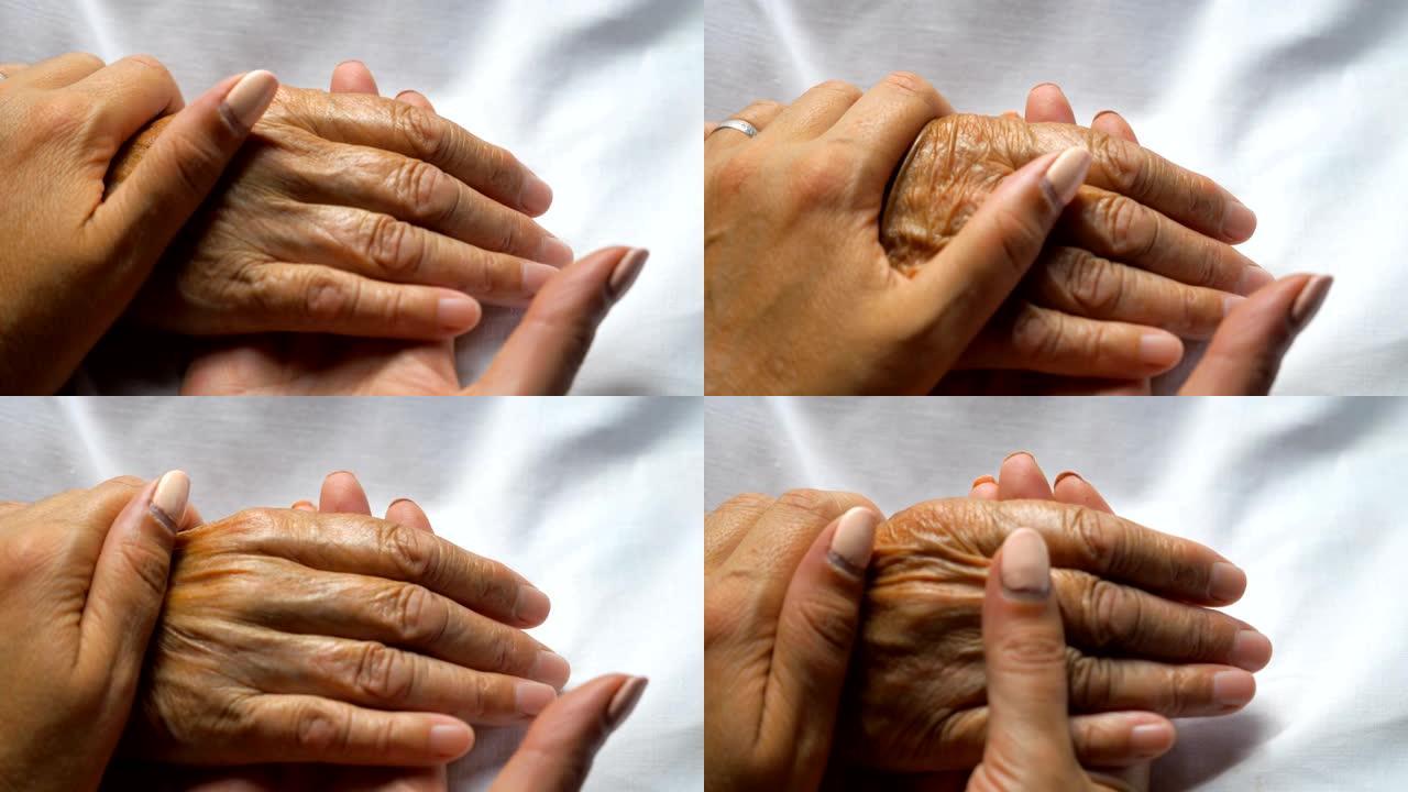 女人握着并轻轻地抚摸着母亲的手，表现出关怀或爱心。女儿安慰躺在诊所床上的年迈妈妈的皱纹手臂。支持她的