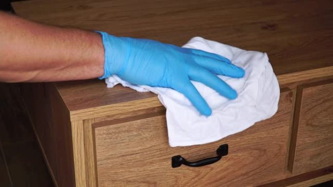 一个戴着蓝色手套的男人用抹布在床头柜上洗家具。防止冠状病毒传播和感染新型冠状病毒肺炎。如何防止冠状病