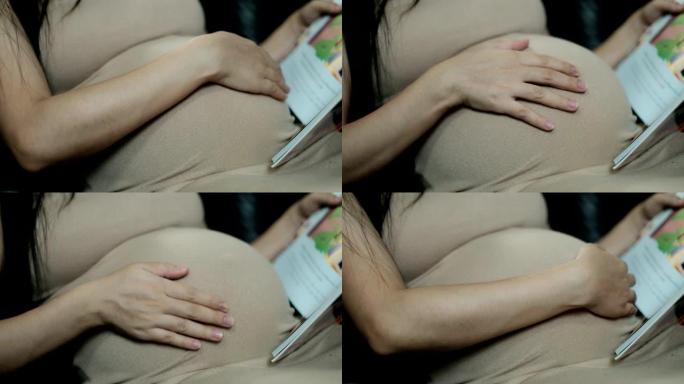 穿着衣服的孕妇的特写镜头把手放在肚子上。
读卡通书籍给肚子里的孩子听。