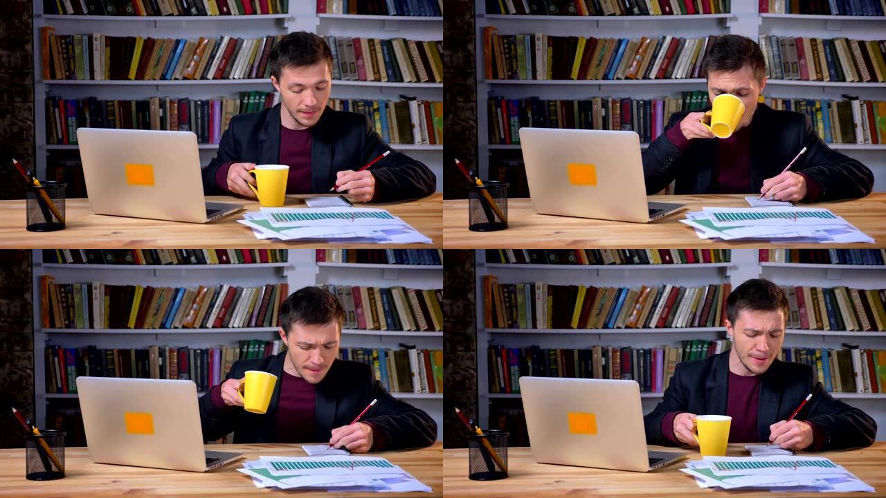 有吸引力的男学生做笔记，使用笔记本电脑并在图书馆学习