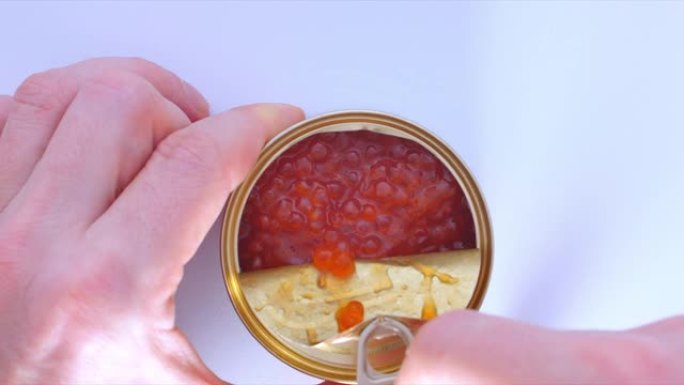 男人的手从一罐红色鱼子酱中打开盖子。顶视图。用红色鱼子酱打开罐子。健康食品的概念，没有转基因生物，没