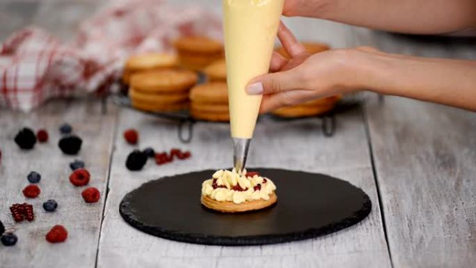 糕点厨师用奶油冻和浆果制作法国Mille Feuille。法式甜点油酥和奶油。