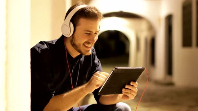 男人在晚上戴着耳机在平板电脑上浏览