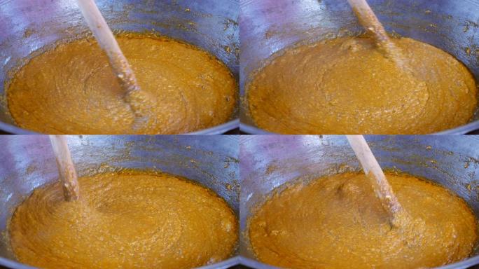 老妇人用大木勺慢动作在大烤箱里搅拌蒸年糕 (泰国甜点)