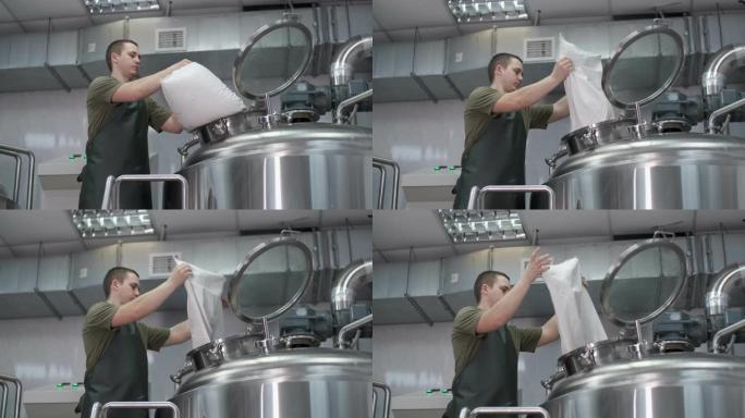 一个工作的男性酿酒商将压碎的麦芽倒入啤酒罐中，以生产精酿啤酒。特写