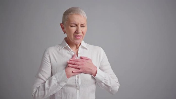 老年妇女在灰色背景上心脏病发作。老年妇女有胸痛