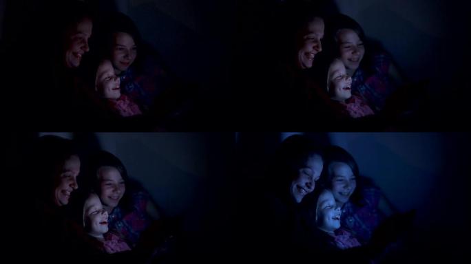 一个小女孩和妈妈躺在床上，在智能手机屏幕、儿童和数字技术上观看动画片。儿童和父母的家庭关系