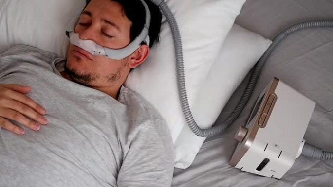 oung成年男子戴着鼻面罩 (CPAP面罩) 并使用CPAP机睡觉