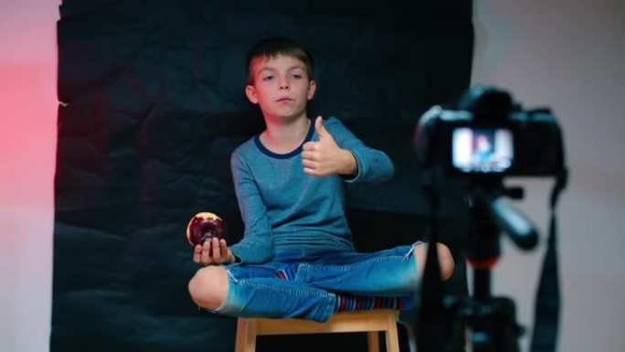 一个男孩正在摄像机前吃一个红苹果。
