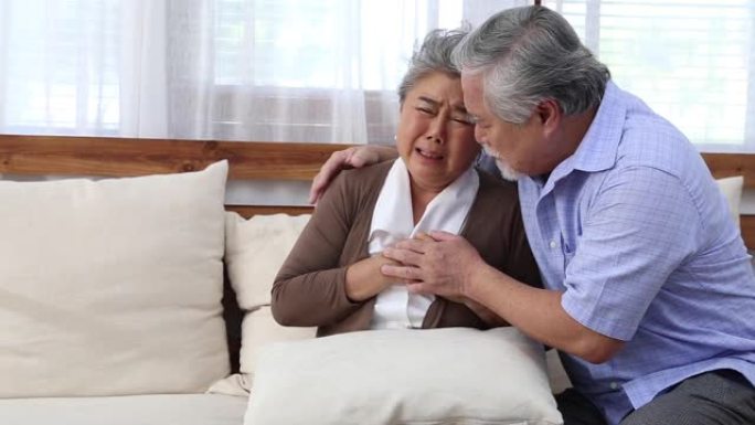 亚洲高级女性在客厅沙发上心痛，由丈夫照顾，健康问题和不适