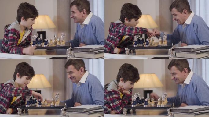 白人小男孩和中年男子下棋。祖父和孙子一起在家过夜。生活方式、休闲、爱好
