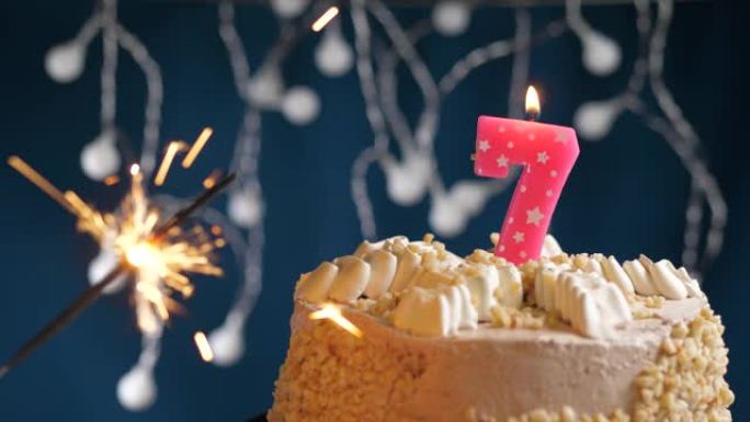 生日蛋糕，7号粉色蜡烛和蓝色背景上的烟火。慢动作和特写视图