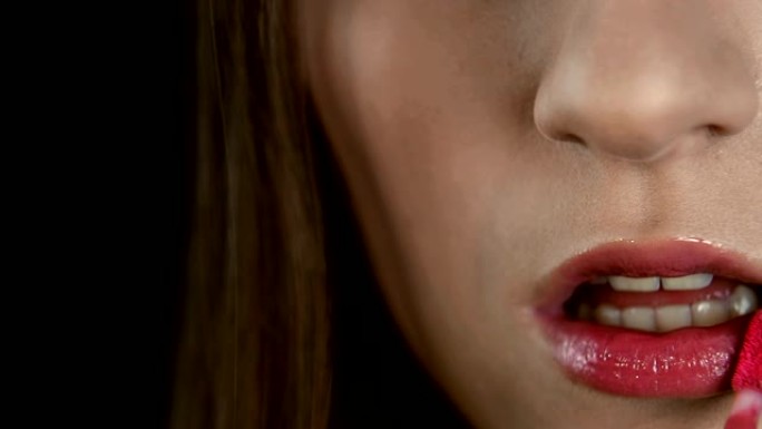 艺术家的手化妆，画出女孩的嘴唇特写。骨头用红色唇膏涂她的嘴唇。在时尚美容行业工作的模特